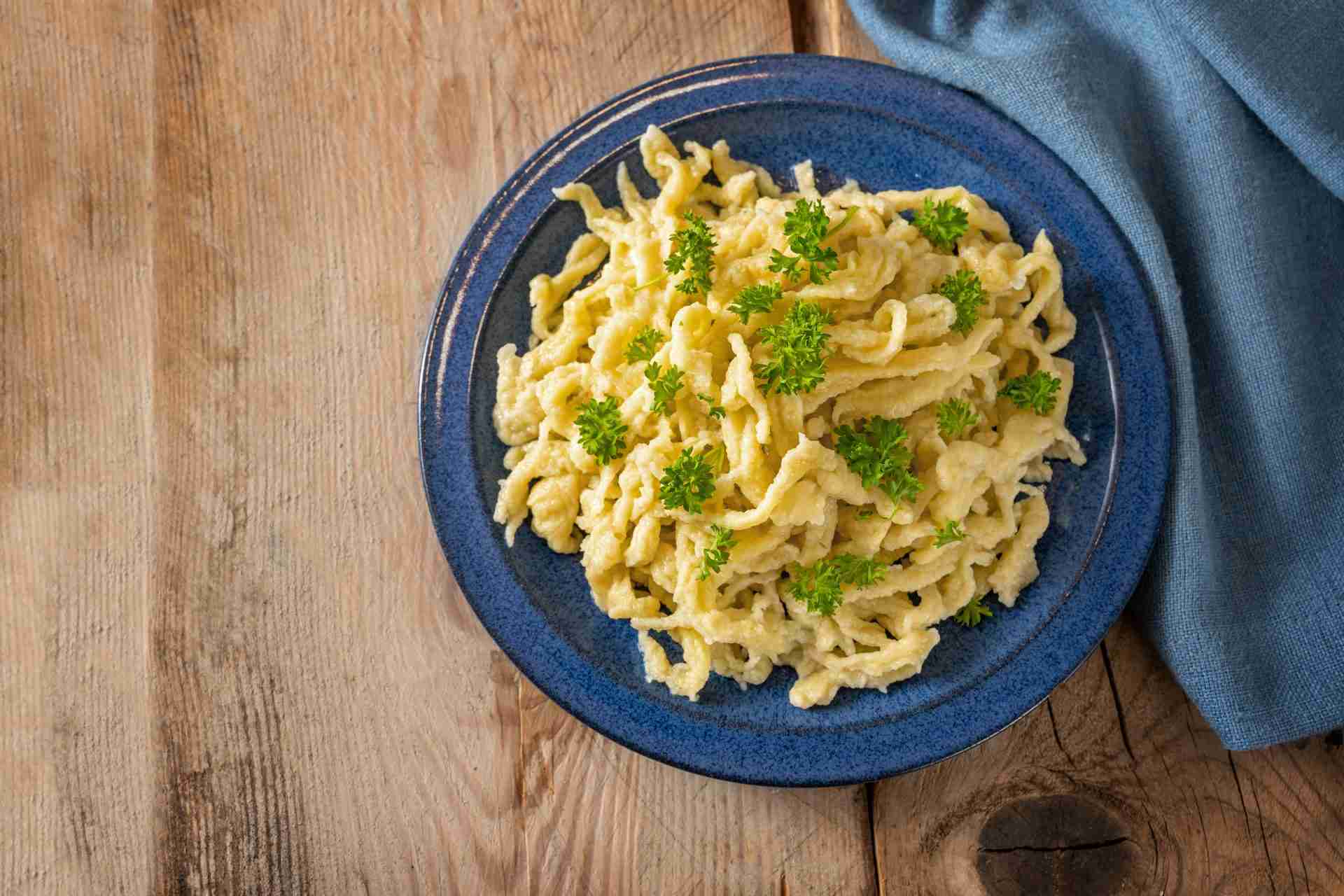 Spaetzle, homemade egg noodles with parsley garnish on a blue plate and a rustic wooden table with copy space, traditional dish in Schwaben, southern Germany and Austria
