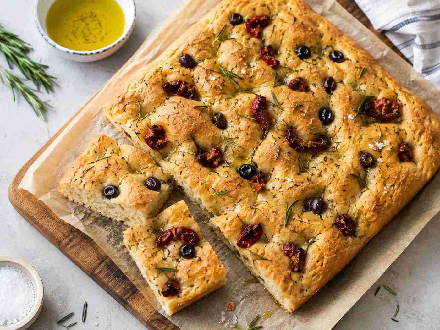 Homemade focaccia with olive oil, coarse salt, rosemary, tomatoes, and olives